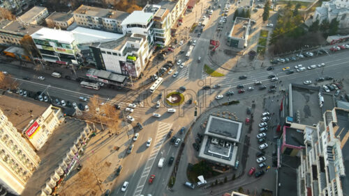 Video - CHISINAU, MOLDOVA - JANUARY 15, 2021: Aerial drone view of city at sunset. Multiple residential buildings, stores, road with roundabout and moving cars. Bare trees, winter