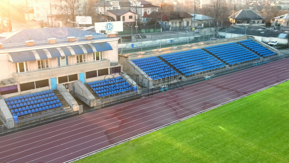 Video - CHISINAU, MOLDOVA - JANUARY 15, 2021: Aerial drone view of Dinamo Stadium with tribunes, green grass, run paths, road on the background. Bare trees, winter