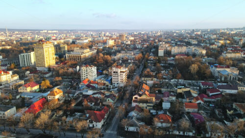 Video - Aerial drone view of Chisinau at sunset. Panorama view of multiple buildings, road with moving car, bare trees. Moldova