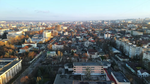 Video - Aerial drone view of Chisinau at sunset. Panorama view of multiple buildings, road with moving car, bare trees. Moldova