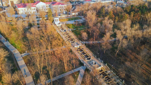 Video - Aerial drone view of Chisinau cascade staircase at sunset. Multiple bare trees, walking people, buildings on the background. Moldova