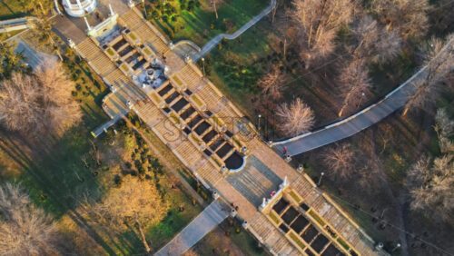 Video - Aerial drone view of Chisinau cascade staircase at sunset. Multiple bare trees, walking people. Moldova