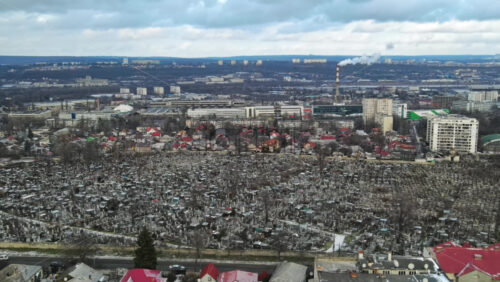 Video - Aerial drone view of a cemetery in Chisinau, Moldova. Multiple graves, crypts, walkways. Cityscape on the background. Cloudy weather, bare trees, winter