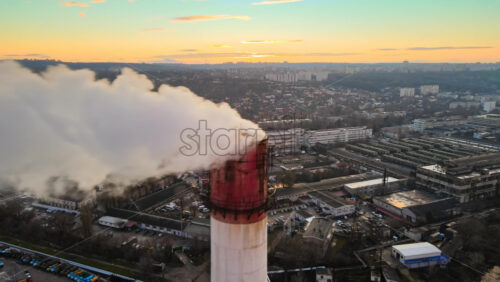 Video - Aerial drone view of Chisinau at sunset. Tube of the thermal station with smoke coming out. Industrial zone near it and cityscape on the background. Moldova