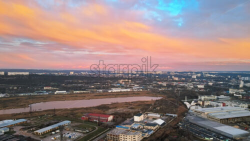 Video - Aerial drone view of Chisinau at sunset. Panorama view of industrial zone, residnetial buildings, lake, bare trees. Rose clouds