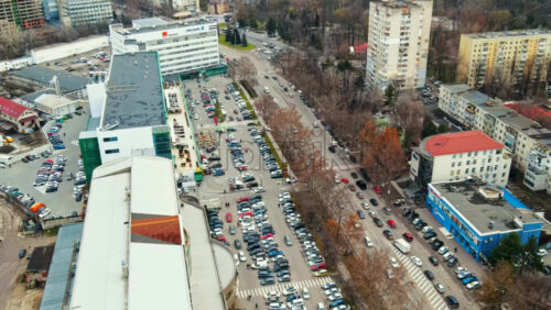 Video - Aerial drone view of Chisinau. View of multiple buildings, road with moving cars, parking and bare trees along the street. Moldova