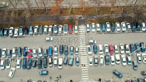 Video - Aerial drone view of Chisinau. View of a parking near a mall, road with moving cars, walking people and bare treest. Moldova