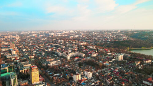 Video - Aerial drone view of Chisinau at sunset. Multiple buildings, trees, park with a lake, setting sun. Moldova