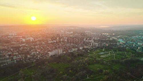 Video - Aerial drone view of Chisinau at sunset. Multiple buildings, trees, park, setting sun. Moldova