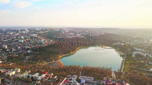 Video - Aerial drone view of Chisinau at sunset. Multiple buildings, trees, park with a lake, setting sun. Moldova