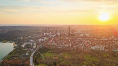 Video - Aerial drone view of Chisinau at sunset. Multiple buildings, trees, park with a lake, road with moving cars, setting sun. Moldova