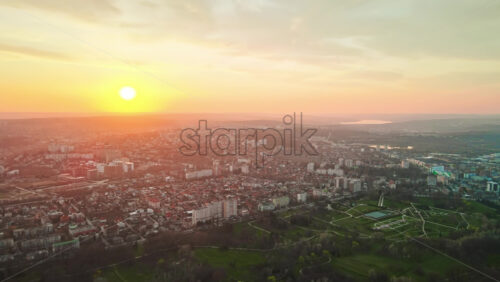Video - Aerial drone view of Chisinau at sunset. Multiple buildings, trees, park, setting sun. Moldova
