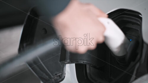 Video - Man plugging in charger into an electric car, blue flickering light in the socket. Slow motion