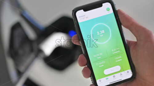 Video - Man charging electro car, holding smartphone with charging process status