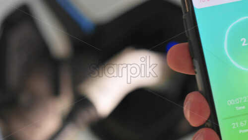 Video - Man charging electro car, holding smartphone with charging process status