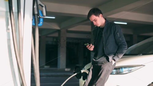 Video - Man using smartphone and staying near his charging electric car