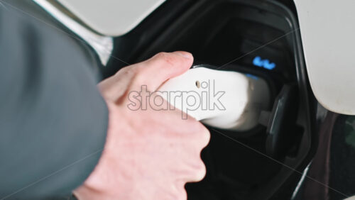 Video - Man plugging in charger into an electric car, blue flickering light in the socket. Slow motion