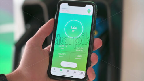 Video - Man charging electro car, holding smartphone with charging process status