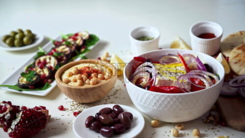 Video - Close-up view of a table full of healthy national food in dishes. Sliced vegetables, salads and appetizers. A man filling the salad with olive oil. Slow motion