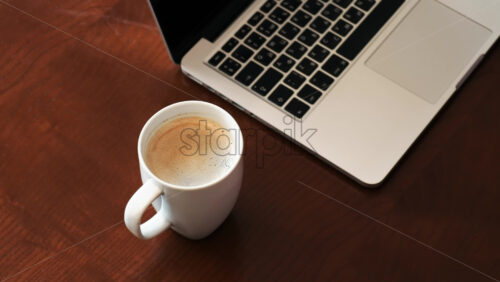 Video - A man puts a cup of coffee, laptop on the wooden table. Top view