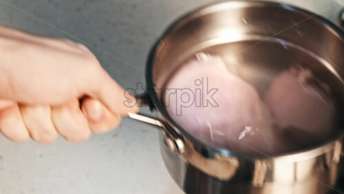 Video - A man puts the chicken breast in a saucepan with water on the stove