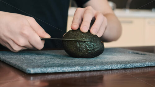 Video - A man slicing an avocado using a knife on a cooking board