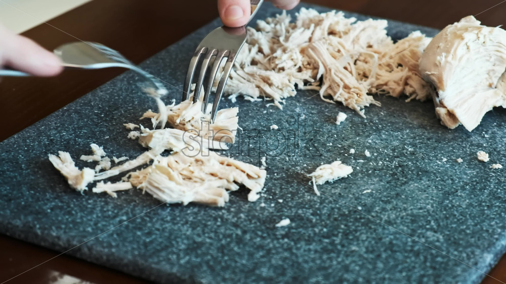Video - A man slicing boiled chicken breast on a cooking board using two forks