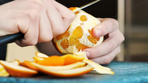 Video - A man peeling an orange using a knife on a cooking board