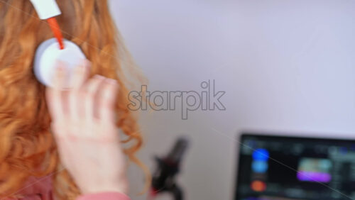 Video - Young content creator girl editing video on her laptop with headphones. Microphone and camera lens on table. Working from home