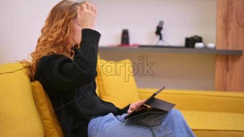Video - Young content creator using her tablet on yellow sofa. Cozy environment for working from home