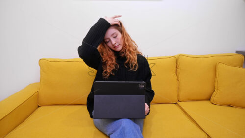 Video - Young content creator using her tablet on yellow sofa. Cozy environment for working from home