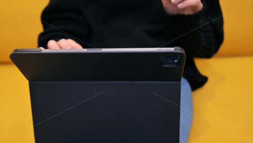 Video - Young content creator using her tablet on yellow sofa. Cozy environment for working from home. Close up typing