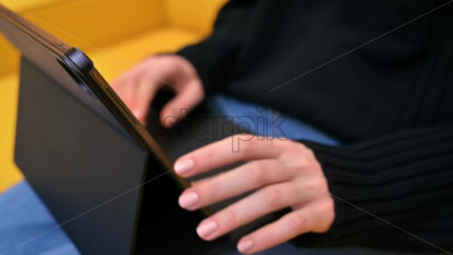 Video - Young content creator using her tablet on yellow sofa. Cozy environment for working from home. Close up typing