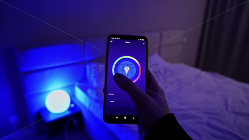 Video - Woman hands holding smartphone, changing color light in hue app in the bedroom. Smart home