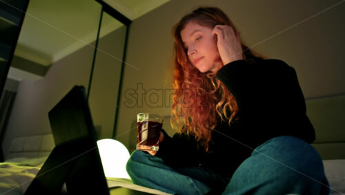 Video - Young ginger hairl girl using her tablet in the bedroom, drinking coffee and changing light color in hue app. Working from home