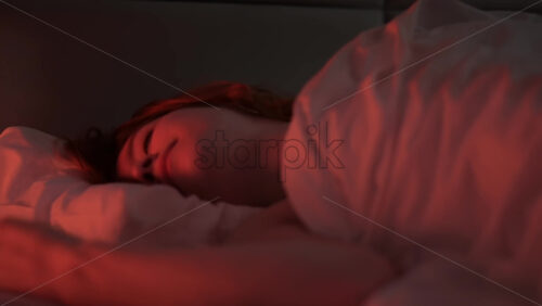 Video - Young ginger hair girl browsing her smartphone at night in the bed. Trying to fall asleep. Colorful light