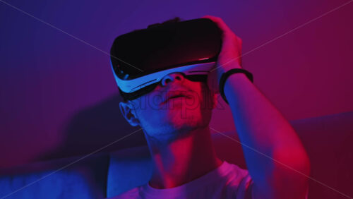 Video - Young man using virtual reality headset in the bedroom at night. Colorful neon lights