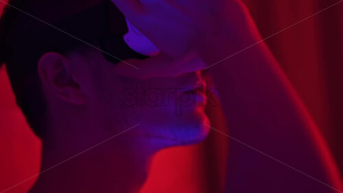 Video - Young man using virtual reality headset in the bedroom at night. Colorful neon lights