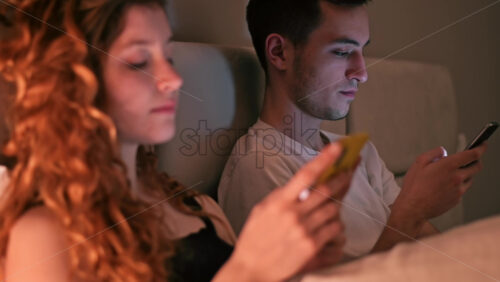 Video - Young couple using smart phones at night in the bed. Colorful light