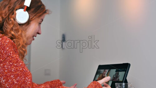 Video - Young ginger girl with headphones talking to her friends in video conference. Group of young people working from home
