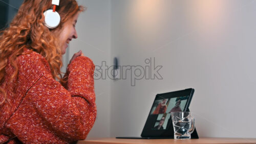 Video - Young ginger girl with headphones talking to her friends in video conference. Group of young people working from home