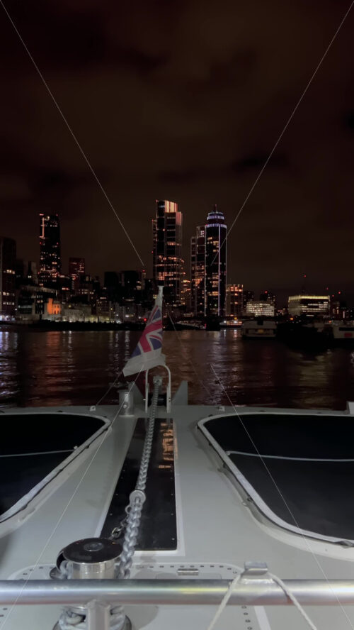 Video - The flag of the United Kingdom waving on a boat moving on the Thames River in the evening in London, England. Vertical