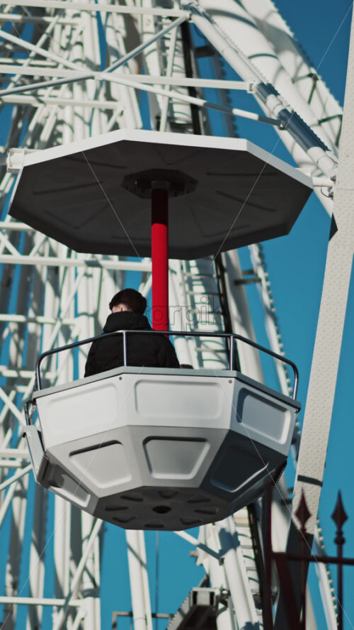 Video - Close up of people in a cabin in a Ferris Wheel with the blue sky on the background. Vertical