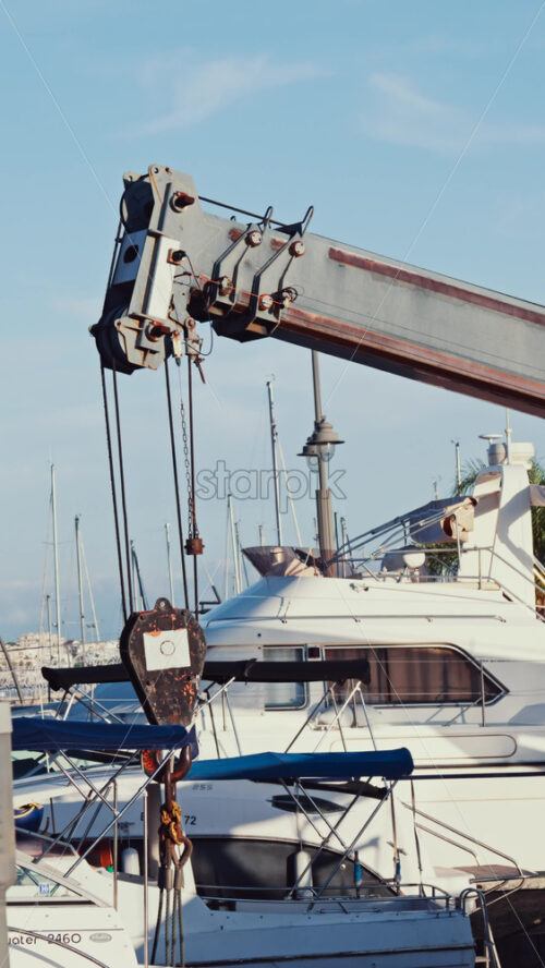 Video - A crane machine moving down near boats docked in a harbour. Vertical