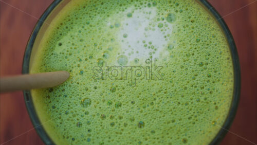 Video - Close up of a matcha latte with a paper straw on a wooden table