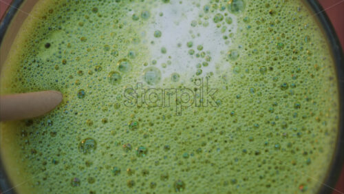Video - Close up of a matcha latte with a paper straw on a wooden table