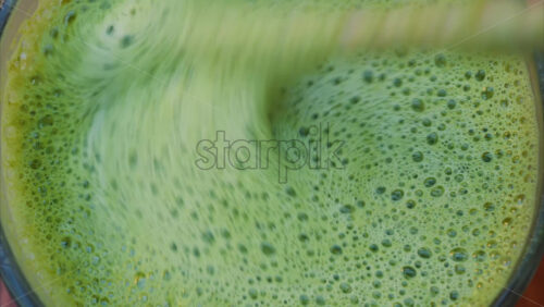 Video - Close up of a woman mixing a matcha latte with a paper straw at a cafe