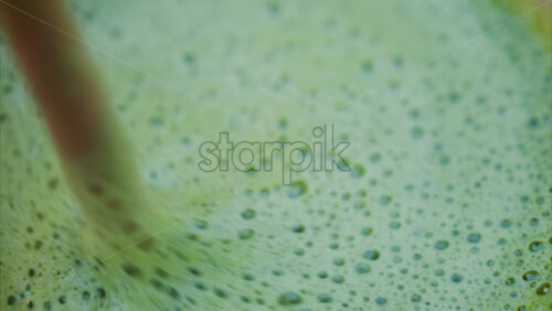 Video - Close up of a woman mixing a matcha latte with a paper straw at a cafe