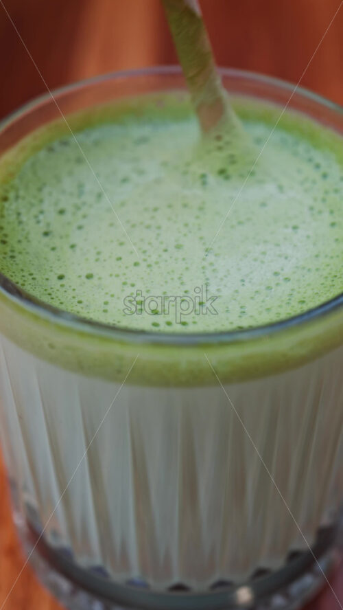 Video - Close up of a woman mixing a matcha latte with a paper straw at a cafe. Vertical