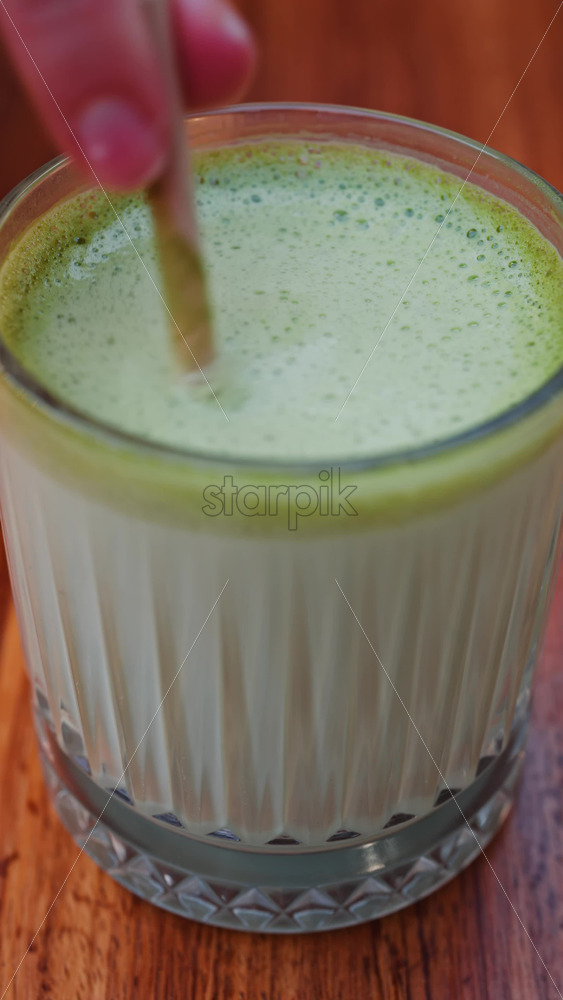 Video - Close up of a woman mixing a matcha latte with a paper straw at a cafe. Vertical